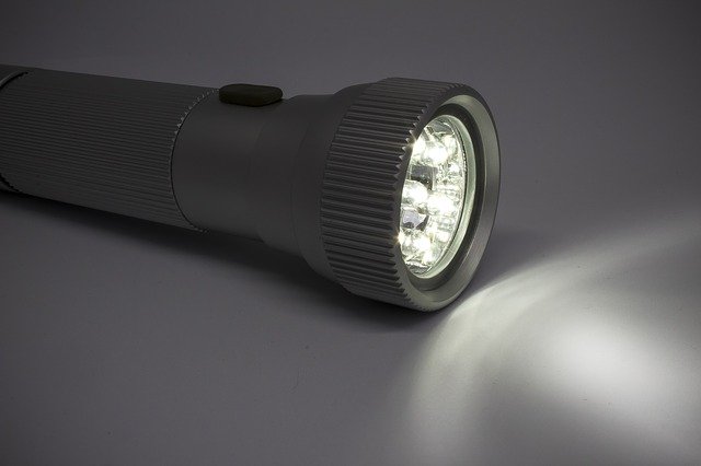 Utensilien gegen Stromausfall, großes Bild mit brennender, leuchtender LED-Taschenlampe liegt auf dem Tisch