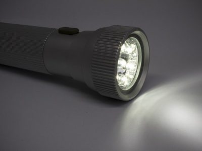 Utensilien, leuchtende Taschenlampe Utensilien gegen Stromausfall, großes Bild mit brennender, leuchtender LED-Taschenlampe liegt auf dem Tisch